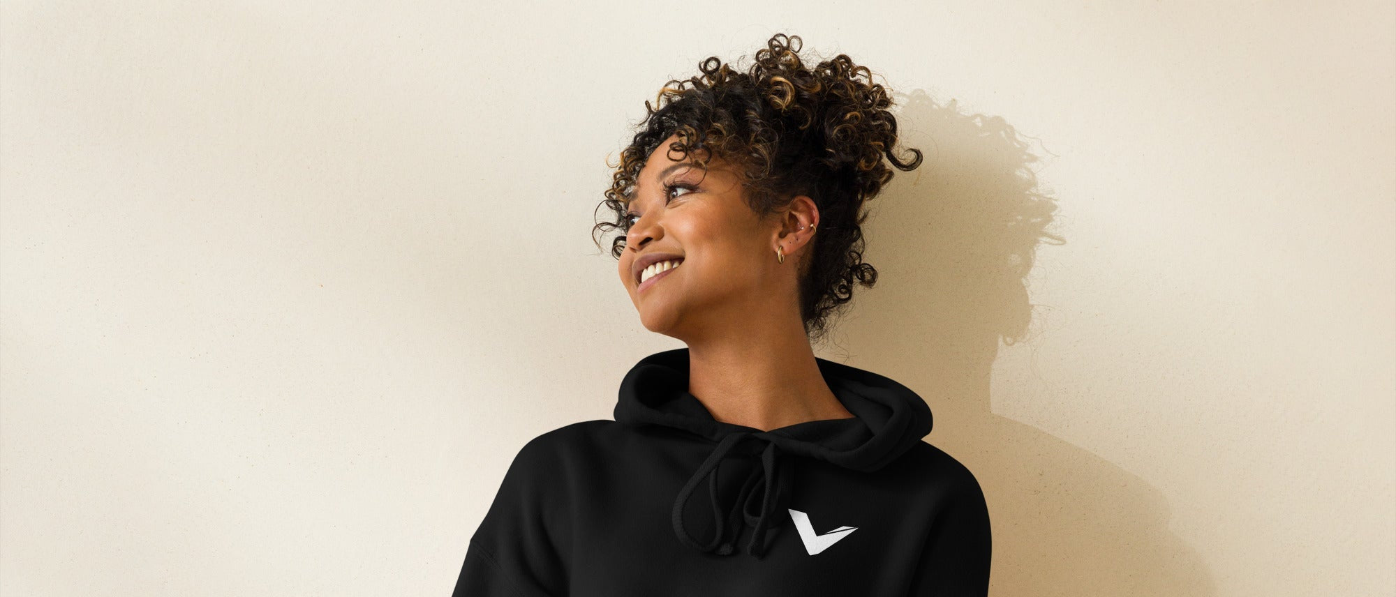 Woman wearing a black hoodie and teal shorts against a beige background